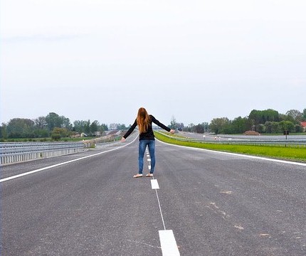 Picture of a girl with long red hair holding her hands out staring down a long deserted road